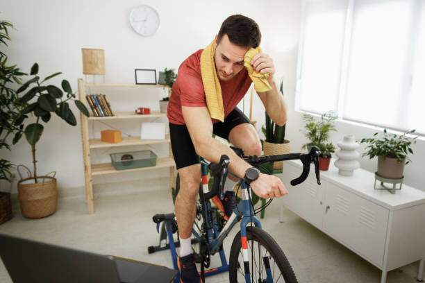 istock Young handsome man exercising on bike at home while using laptop 1812072843