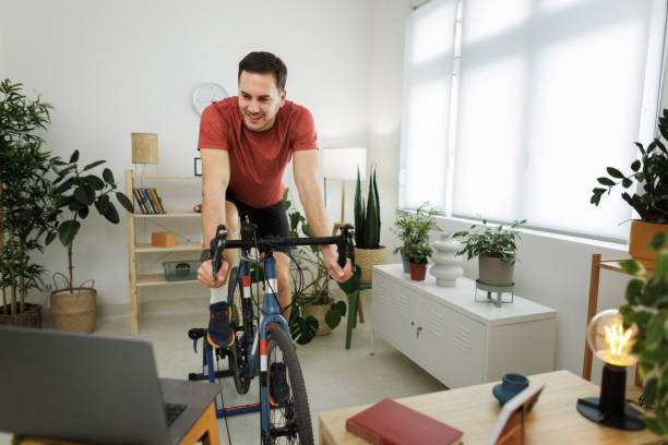 istock Handsome athletic man riding exercise bicycle at home 1812073382