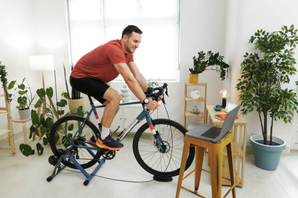 istock Handsome athletic man riding exercise bicycle at home 1812073384