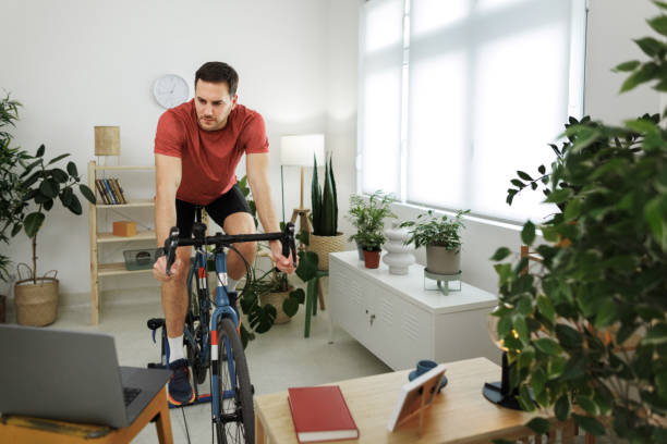 istock Handsome athletic man riding exercise bicycle at home 1812073385
