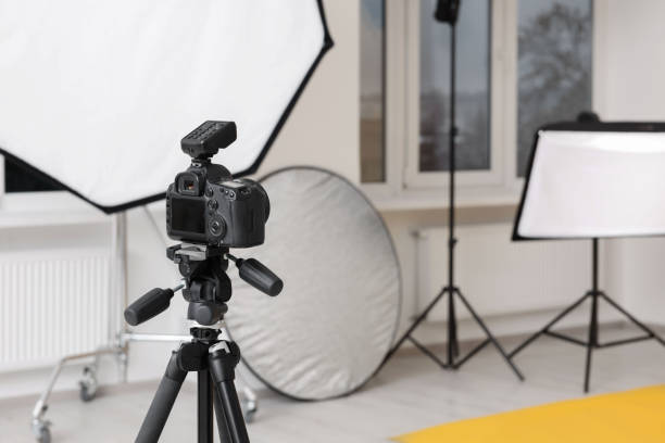 istock Camera on tripod and professional lighting equipment in modern photo studio, space for text 1812073389