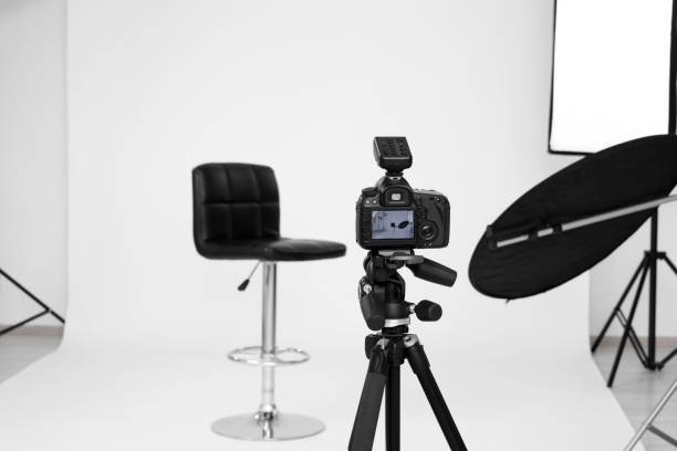 istock Camera on tripod, bar stool and professional lighting equipment in modern photo studio, space for text 1812074476