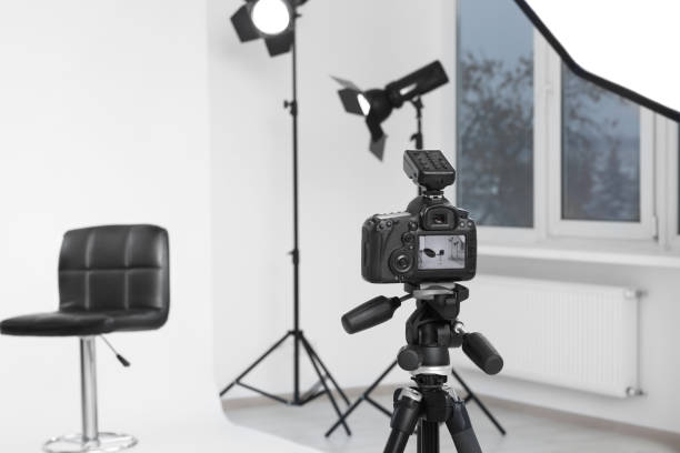 istock Camera on tripod, bar stool and professional lighting equipment in modern photo studio, space for text 1812075012