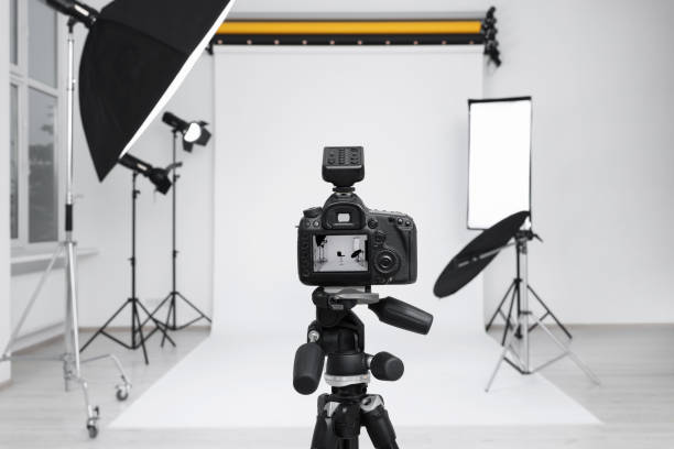 istock Camera on tripod, bar stool and professional lighting equipment in modern photo studio 1812075028