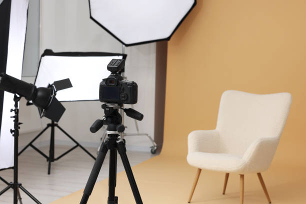 istock Camera on tripod, armchair and professional lighting equipment in modern photo studio, space for text 1812076708