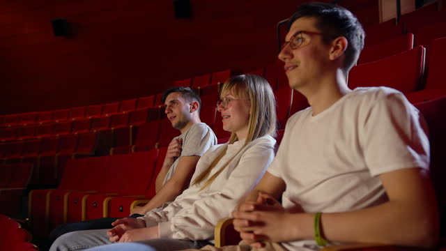 Adolescent friends watch a scary movie on the big screen, side view