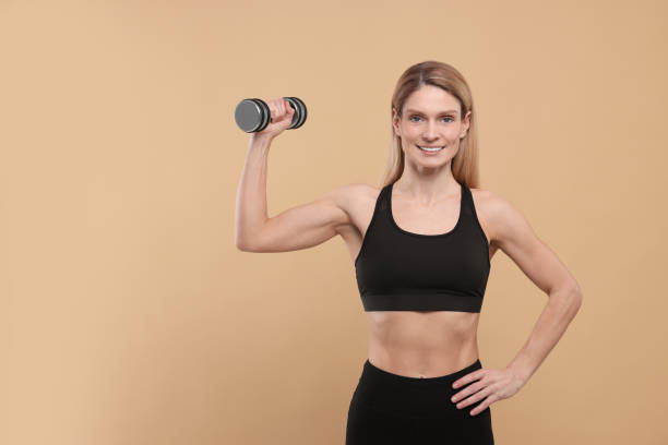 istock Athletic woman exercising with dumbbell on beige background, space for text 1812101046