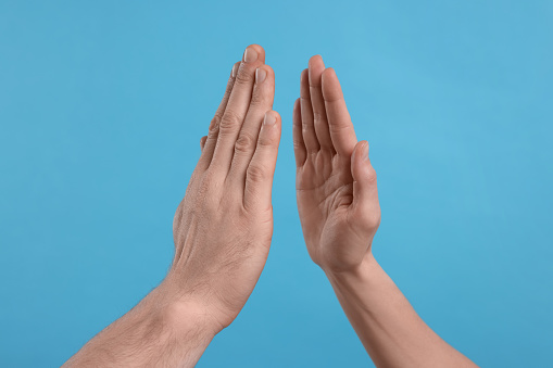 People giving high five on light blue background, closeup