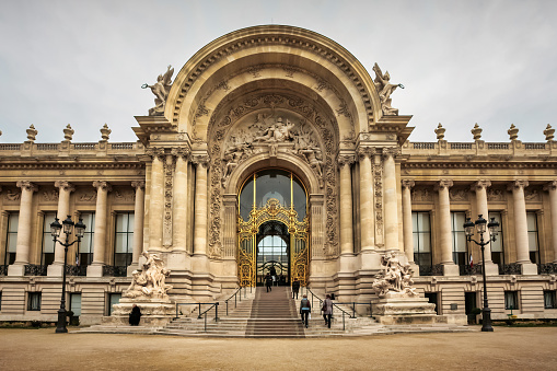 Pedestrians walk in front of The Petit Palais in Paris, France on an overcast day. The Petit Palais was built World Expo 1900, it now houses the City of Paris Museum of Fine Arts.