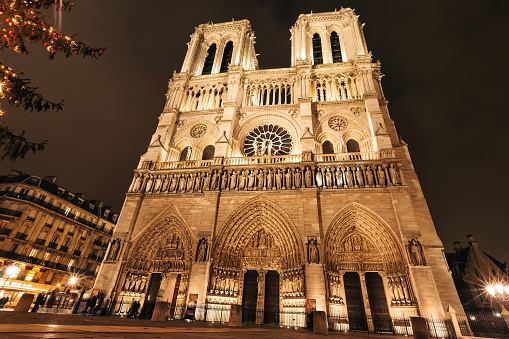 People stand in front of the Notre Dame cathedral in Paris, France at night.