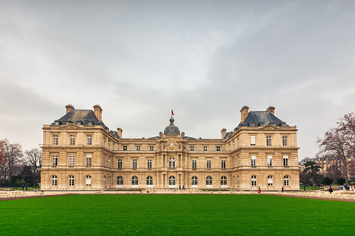 Pedestrians walk in front of Palais du Luxembourg, Luxembourg Palace in Paris, France on a cloudy day.