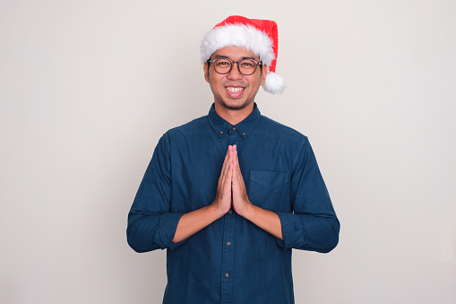 A man wearing christmas hat doing greeting gesture with happy expression