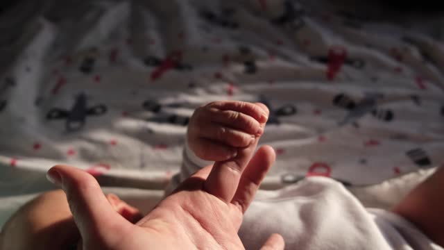 Women's, mother's hand holding a small hand of a newborn baby or child