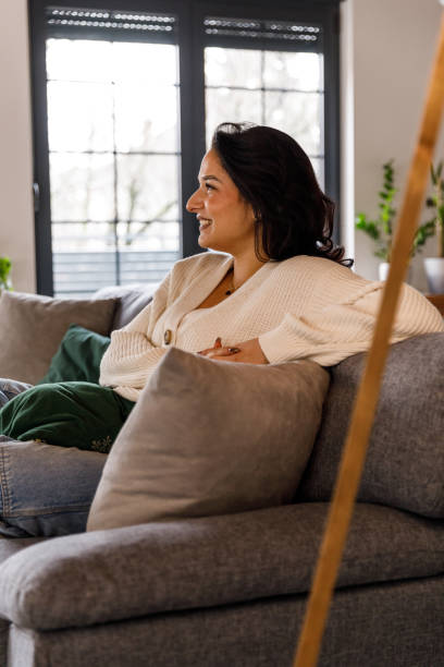 istock Young woman lounging on the sofa, smiling, daydreaming 1812238778