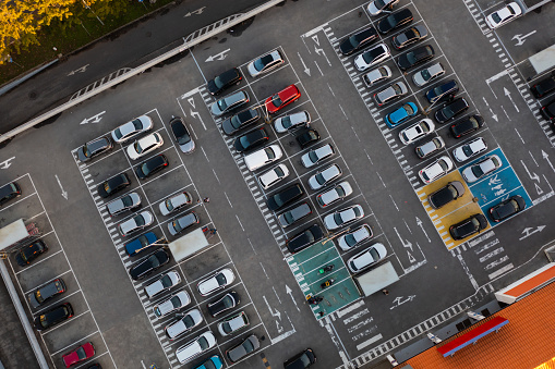 Aerial view of large parking lot in front shopping mall with many parked cars in European city. Carpark at supermarket with lines and markings for vehicle places and directions