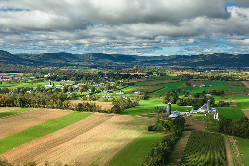 Drone shot of farms surrounded by rolling green fields in Lycoming County, Pennsylvania on a sunny day in Fall. The area is known for a large number of Mennonite and Amish communities.