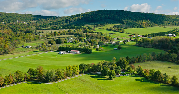 Drone shot of farms surrounded by rolling green fields in Lycoming County, Pennsylvania on a sunny day in Fall. The area is known for a large number of Mennonite and Amish communities.