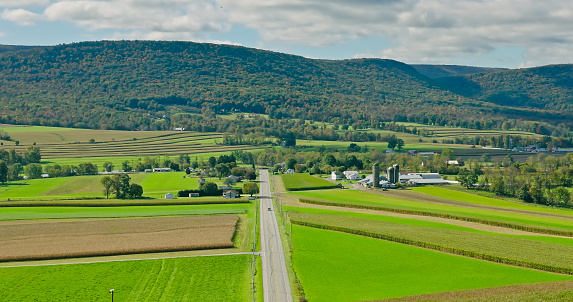 Drone shot of farms surrounded by rolling green fields in Lycoming County, Pennsylvania on a sunny day in Fall. The area is known for a large number of Mennonite and Amish communities.