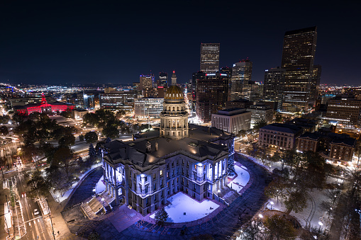 Aerial still image of the Colorado State Capitol building, with downtown Denver in the background, taken by a drone on a snowy night in Denver.