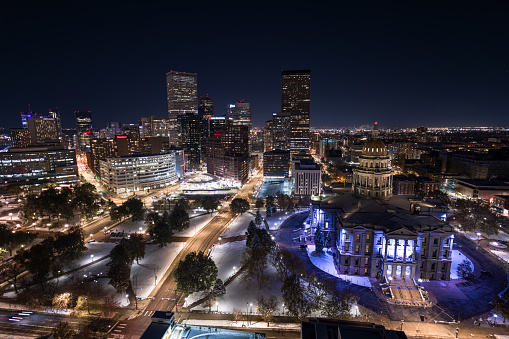 Aerial still image of the Colorado State Capitol building, with downtown Denver in the background, taken by a drone on a snowy night in Denver.