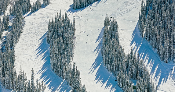 Aerial still image of people skiing and snowboarding down a hill at a ski resort on a cold, sunny morning near Loveland Pass, Dillon, Colorado.