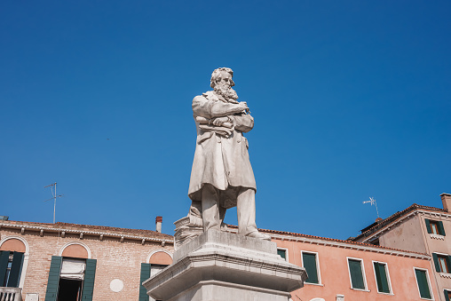 A striking statue of a man in a long coat and hat stands in front of a building in Venice, Italy, adding to the city's rich history and charm.