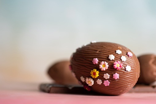 Easter decoration. Chocolate egg decorated with small multicolored flowers on a pastel blue background