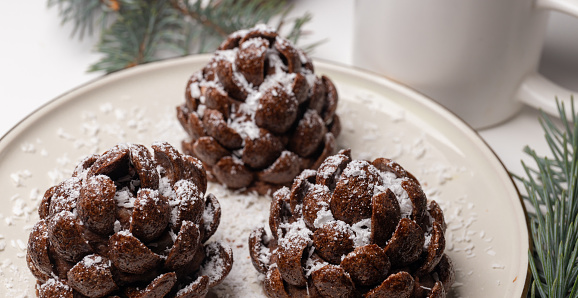 Christmas tree cone-shaped cookies with chocolate flakes with powdered sugar, a delightful homemade dessert for the New Year. These chocolate pine cone-shaped shortbread cookies with sweet snow.