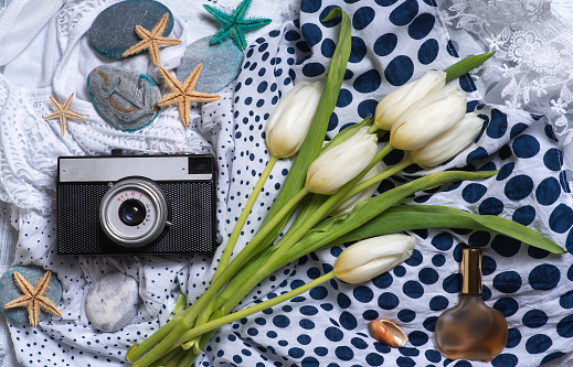 A bouquet of white tulips and old analog photo camera on a lace dress