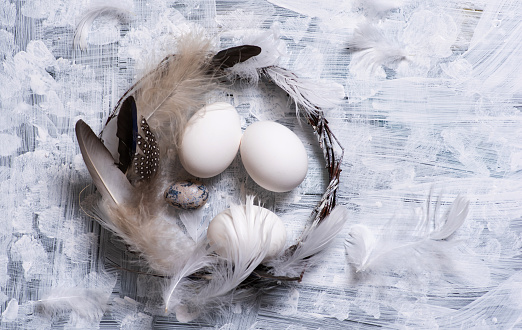 White eggs in a wreath of dry branches decorated with colorful natural feathers on white background