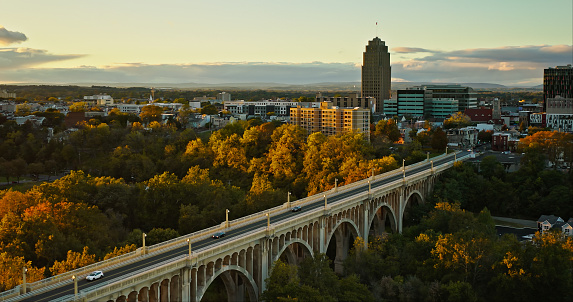 Aerial establishing shot of Allentown, Pennsylvania at sunset on Fall evening, looking across the Albertus L. Meyers Bridge and St. Paul's Park towards the downtown office buildings. \n\nAuthorization was obtained from the FAA for this operation in restricted airspace.