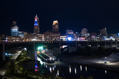 Aerial shot of Cleveland, Ohio from across the Cuyahoga River on a clear night in Fall, with a barge on the Cuyahoga River passing under the Hope Memorial Bridge.