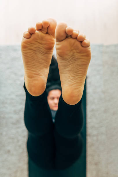 Person sitting cross-legged on a purple yoga mat, feet pressed together, wearing striped pants. Concept of meditation, relaxation, yoga practice, and healthy lifestyle at home.