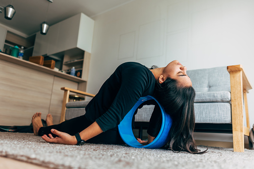 latina woman at home working her back with a yoga wheel.