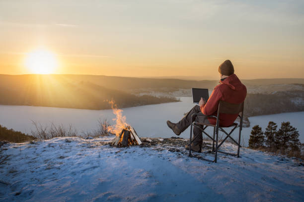 istock man freelancer sitting on snow mountain top using laptop working remotely at sunset. man tourist resting near campfire using laptop. 1812484828