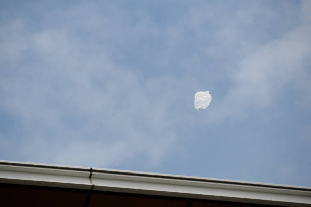 White plastic bag blowing in blue sky wind over a roof