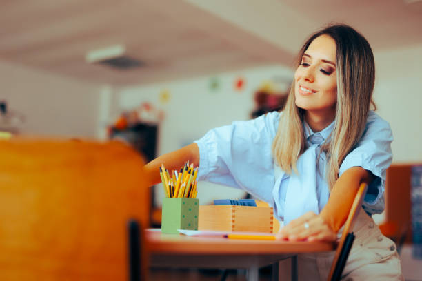istock Happy First Grade Teacher Arranging the Art Supplies for Students 1812572549
