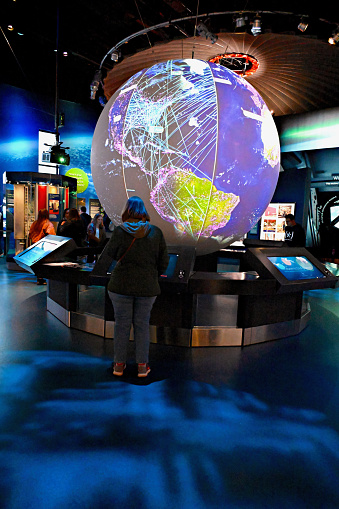 Washington, D.C., USA - November 20, 2023: A visitor to the National Air and Space Museum learns about satellite orbits as she watches a turning globe in the “One World Connected” exhibit.