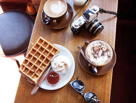 Top down view of table at a cafe in Reykjavik, Iceland. Belgian waffle with butter and jam and two lattes along with a film camera.