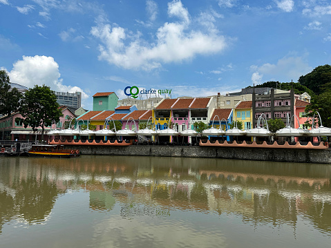 Singapore, Singapore - February 10, 2023: Stock photo showing the colourful shops, bars and restaurants of Clarke Quay reflected in the Singapore River. Clarke Quay was formerly the location of warehouses used to store good transported by light barges from Boat Quay.