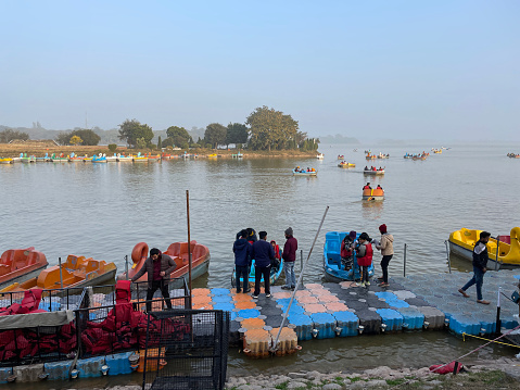 Sukhna Lake, Chandigarh, India - January, 4 2023: Stock photo showing people wearing red life jackets embarking into pedaloes from floating pontoon on Sukhna Lake reservoir, Chandigarh, India.