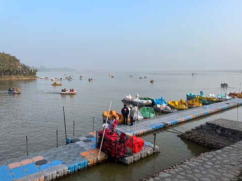Sukhna Lake, Chandigarh, India - January, 4 2023: Stock photo showing people wearing red life jackets in pedaloes from floating pontoon on Sukhna Lake reservoir, Chandigarh, India.