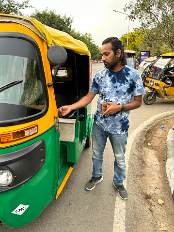 New Delhi, India - March 2, 2023: Stock photo showing close-up view of parked auto rickshaw driver being paid by passenger at end of a ride.