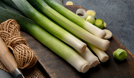 Whole and cut fresh leeks on a dark background, vegetarian food, healthy eating. Top view.