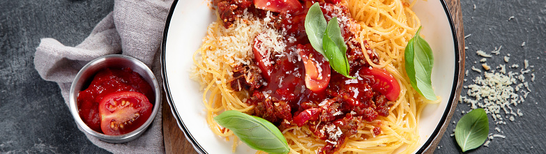 Tasty appetizing classic italian spaghetti bolognese pasta with tomato sauce, cheese parmesan, meat and basil on plate on a dark background. Top view. Panorama, banner.