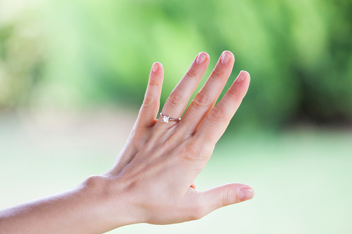 Macro closeup of princess cut diamond engagement ring on woman's female hand showing detail.
