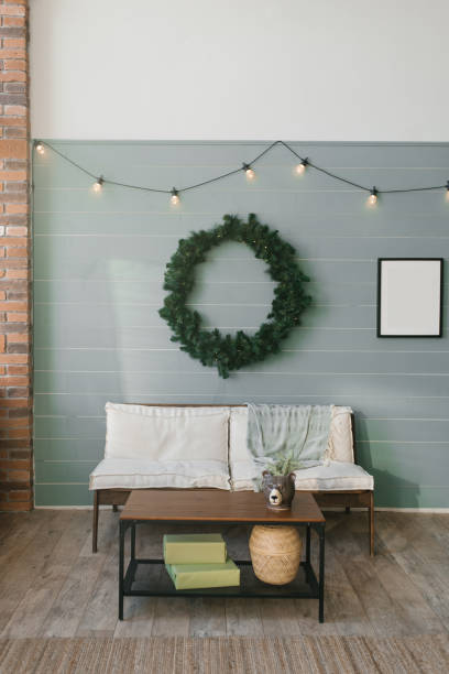 istock Wooden sofa with white soft pillows and a large Christmas wreath on the wall, lined with clapboard, coffee table with Christmas decor 1812815077