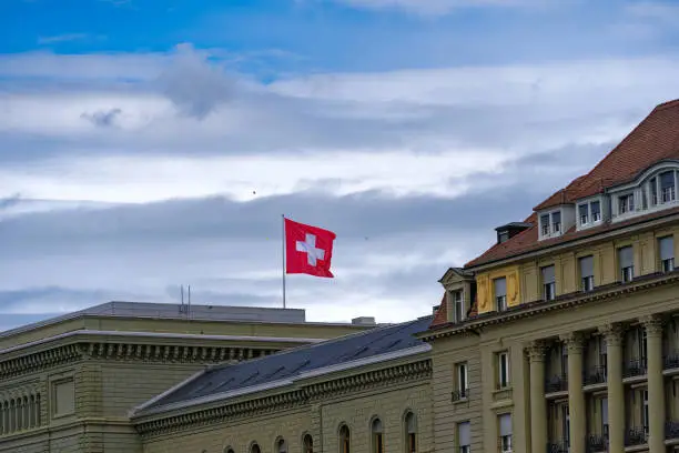 Swiss flag waving at east wing of Swiss Federal Palace at City of Bern on a cloudy summer day. Photo taken July 1st, 2023, bern, Switzerland.