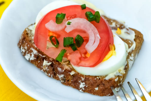 A sandwich with butter, egg and tomato lies on a plate closeup