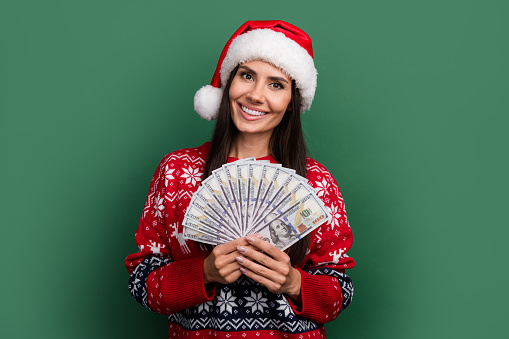 Photo of adorable cheerful lady santa helper dressed print xmas sweater rising money fan isolated green color background.
